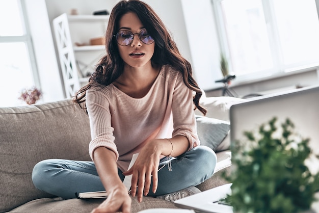 Poner ideas en algo real. Mujer joven pensativa en gafas estudiando mientras está sentado en el sofá en casa