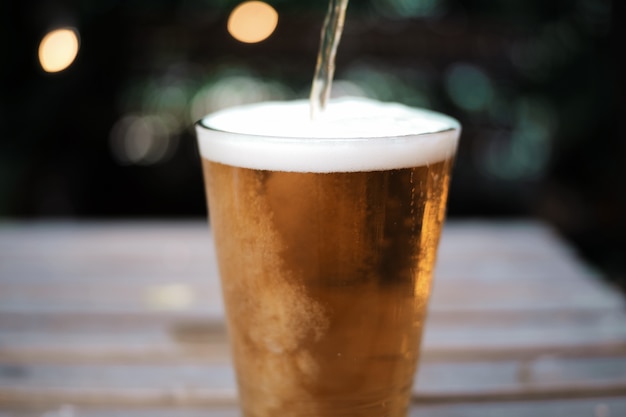 Foto poner mala cara a la cerveza en el vidrio en la tabla de madera en fondo del jardín.