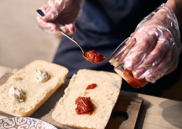 Poner salsa con una cuchara sobre grandes trozos de pan para preparar un sándwich nutritivo según la receta tradicional italiana Cerrar