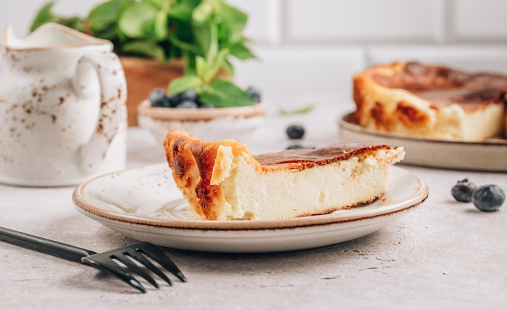 Foto poner un trozo de tarta de queso vasco quemada, toda la tarta al fondo. tarta de queso.