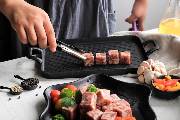 Ponga carne en la plancha, cocinera preparando carne en cubos Wagyu de primera calidad o Saikoro, carne de mármol cortada en cubos para parrilla, tepanyaki o Yakiniku. Enfoque seleccionado