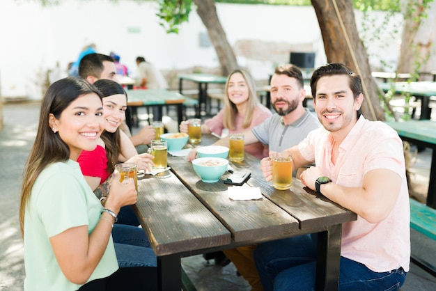 Poniéndome al día con mis amigos. Retrato de un atractivo grupo de amigos de 20 años bebiendo cerveza en un bar al aire libre y disfrutando del tiempo juntos