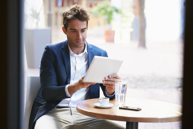 Poniéndose al día con su descanso para tomar café Foto de un joven hombre de negocios disfrutando de una taza de café mientras usa una tableta digital