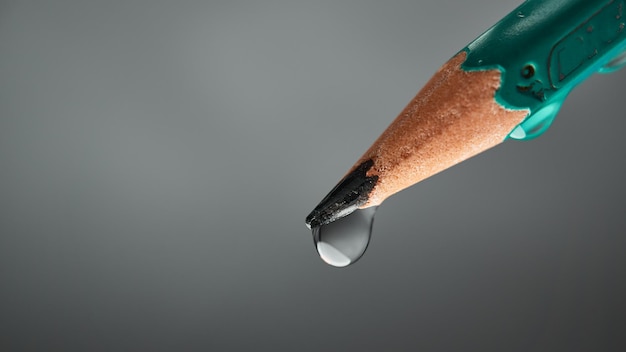 Ponta de um lápis com uma gota no fundo cinza