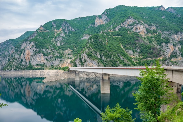 Ponte cruzando um lago com montanhas na parte de trás.