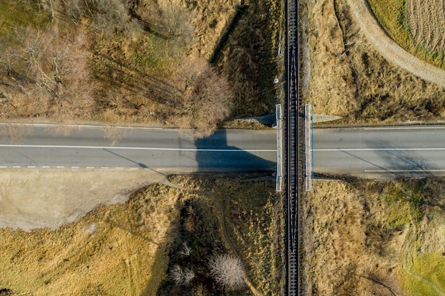 Ponte ferroviária entre prados verdes sobre a estrada na vista aérea do campo