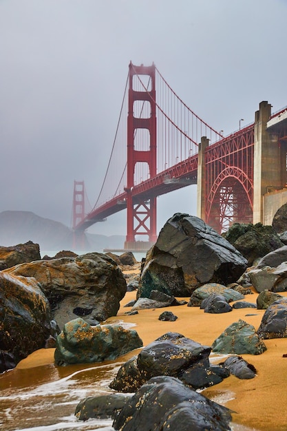 Ponte Golden Gate na manhã nevoenta da praia coberta de rochas