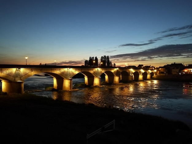 Ponte iluminada sobre o rio contra o céu ao anoitecer
