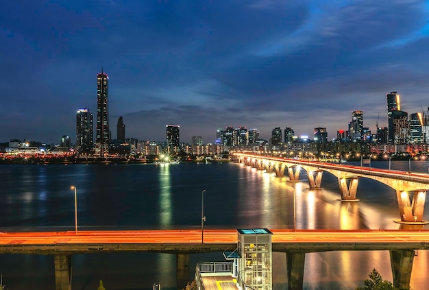 Ponte iluminada sobre o rio por edifícios contra o céu à noite