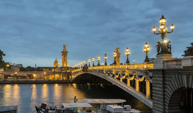 Ponte Pont Alexandre III sobre o rio Sena e Hotel des Invalides ao pôr do sol. Ponte decorada com luminárias e esculturas art nouveau ornamentadas. Paris, França