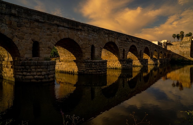 Ponte romana de Mérida iluminada pela luz do sol do crepúsculo refletindo a ponte na água escura