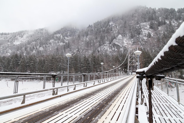 Ponte suspensa de metal para carros e pedestres nas montanhas do Altai no inverno com neve e nevoeiro nas árvores sem pessoas Paisagem de inverno de lugar pitoresco