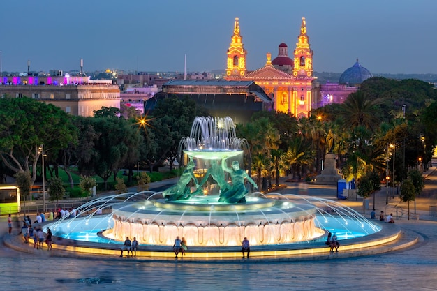 Ponto de referência considerável Triton Fountain, com vários tritões de bronze e a igreja de St. Publius na cidade velha de Valletta, capital de Malta