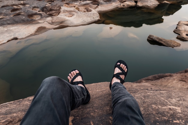 Foto ponto de vista das pernas do homem com tênis de caminhada sentado em um penhasco rochoso no grand canyon
