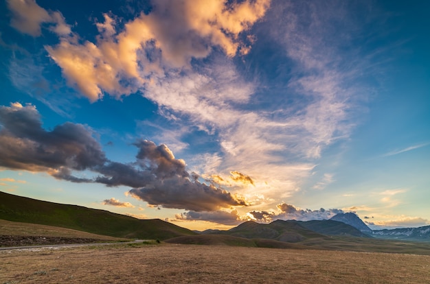 Ponto de vista do pôr do sol em montanhas rochosas, terras altas e pastagens. Campo Imperatore, Gran Sasso, Apeninos, Itália. Nuvens coloridas no céu no cume da montanha dramática.