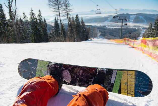 Ponto de vista do snowboarder em pé na encosta nevada sob teleférico em dia de sol nas montanhas