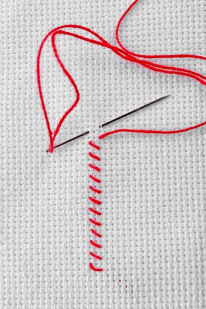 Foto pontos de bordado feitos de linha vermelha e agulha de costura em tecido branco