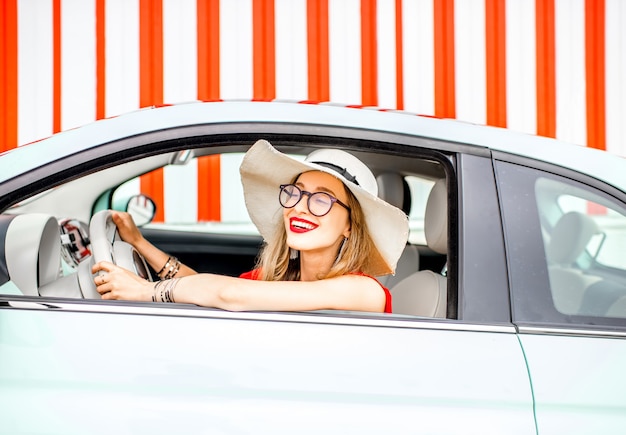 Poortrait einer jungen glücklichen Frau, die während der Sommerferien ein Auto auf dem roten Wandhintergrund fährt