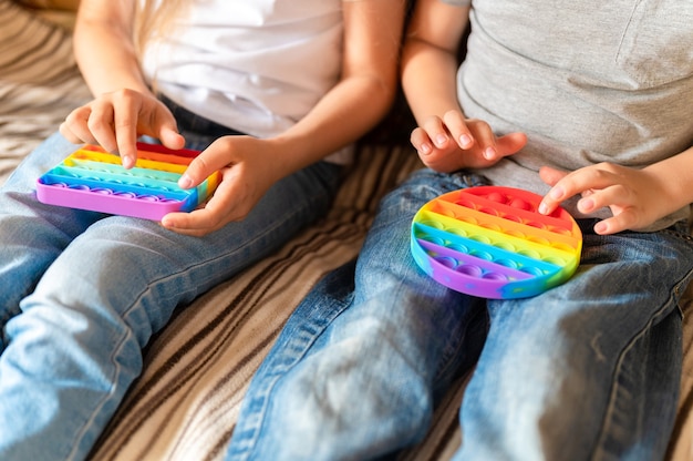 Pop-it sensorial antiestrés juguetes en manos de niños. Unos niños felices juegan con un simple juguete de hoyuelos en casa.