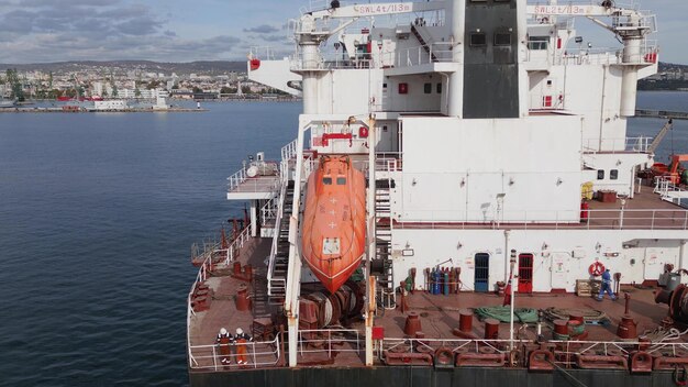 La popa de un buque de carga que sale del puerto con marineros y un bote salvavidas visibles