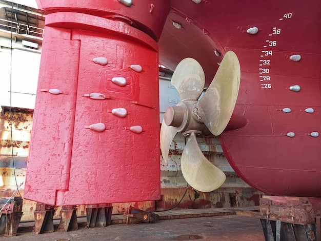 La popa de un gran barco con una hélice de cobre con un aparato de gobierno en una grada en un dique seco