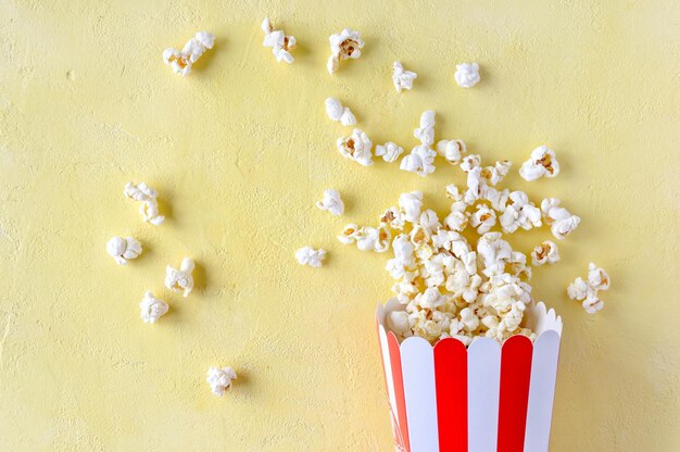 Popcorn fliegt aus einem gestreiften Pappbecher auf gelbem Hintergrund mit Kopierraum Popcorn-Explosion