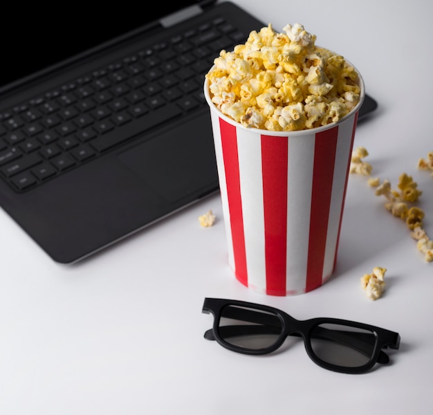 Popcorn im gestreiften roten Eimer, in der 3D-Brille und im Laptop, die Film abspielen.