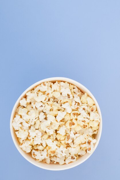 Popcorn in einem Pappbecher ist auf einem pastellblauen Hintergrund, eine Ansicht von oben isoliert. Flach liegen