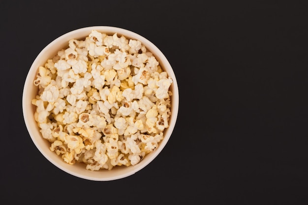 Popcorn in einem Pappbecher ist auf einem schwarzen Hintergrund, eine Ansicht von oben isoliert. Flach liegen