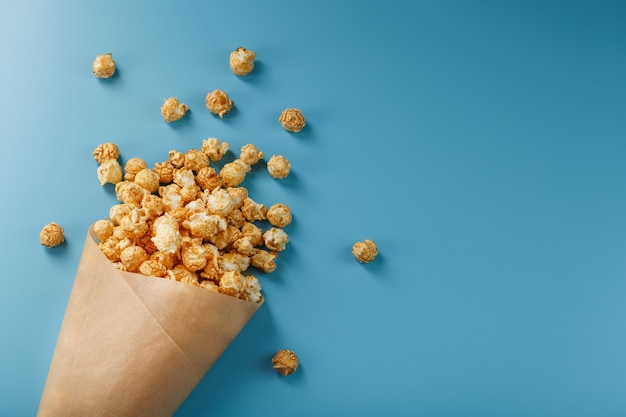 Popcorn in Karamellglasur in einem Papierumschlag auf einem Blau.