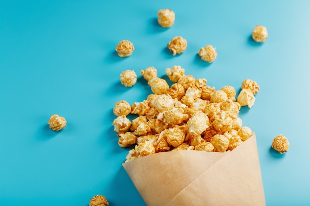 Popcorn in Karamellglasur in einem Papierumschlag auf einem blauen Hintergrund.