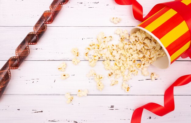 Popcorn, rotes Band auf weißem hölzernem Hintergrund. Valentinstag, Kino.