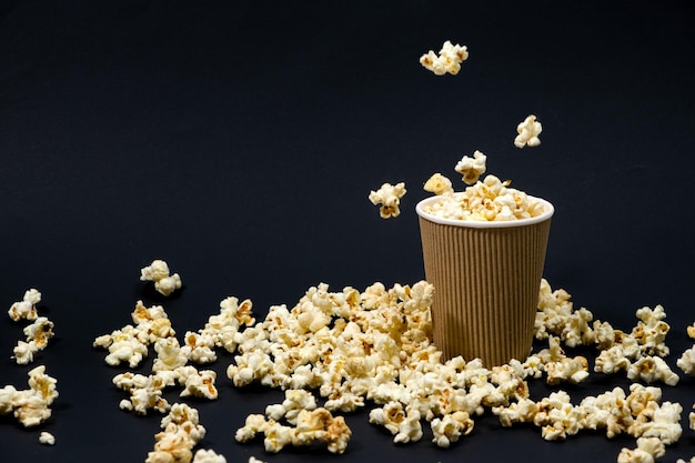 Popcorn wird in ein papierbraunes Glas auf schwarzem Hintergrund gegossen