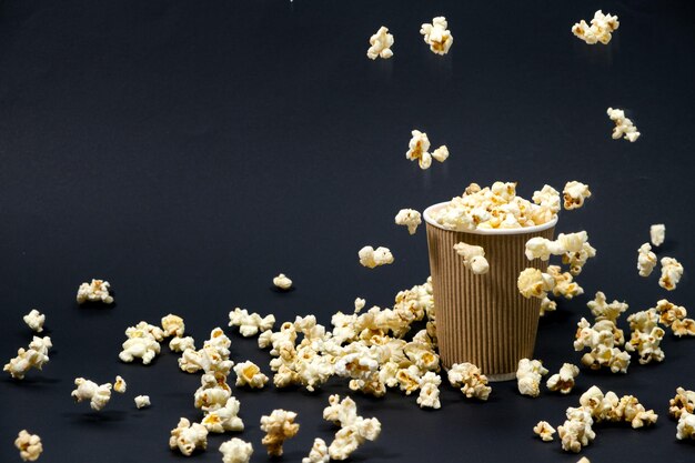 Popcorn wird in ein papierbraunes Glas auf schwarzem Hintergrund gegossen