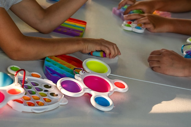 Popit e brinquedos simples entre as mãos de crianças brincando em mesa branca