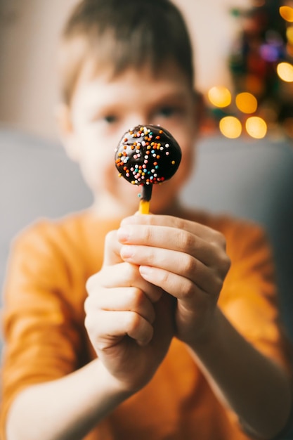 Pops pastel de chocolate con chispitas multicolores primer plano en manos de un niño Merienda dulce en un palo Pastel de chocolate en un palo