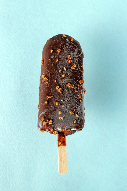 Popsicle mit Nüssen in der Schokolade auf einem selektiven Fokus des blauen Hintergrundes