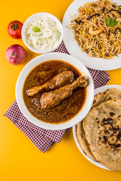 Popular caril de frango avermelhado ou masala, com um pedaço de perna proeminente, servido em uma tigela com arroz Pilau, chapati ou roti e salada