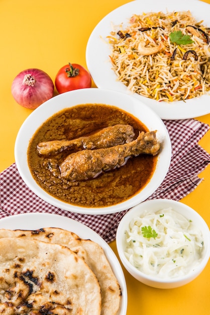 Popular caril de frango avermelhado ou masala, com um pedaço de perna proeminente, servido em uma tigela com arroz Pilau, chapati ou roti e salada