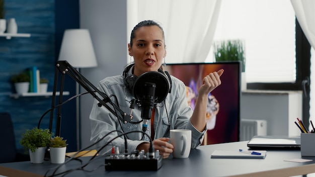 Popular influenciador de Internet ajustando perillas en el controlador de audio mientras filma vlog para plataformas de intercambio de videos. Influenciador de las redes sociales sentado en el escritorio del estudio en casa mientras graba contenido digital.