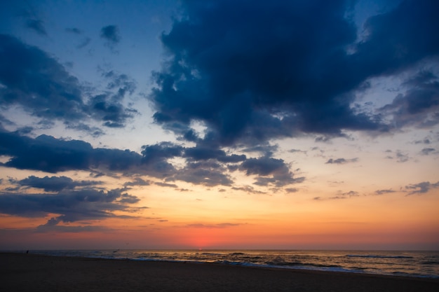 Por do sol bonito em uma praia arenosa vazia. Céu dramático sob o mar.