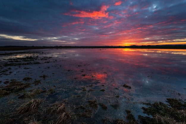 Pôr do sol colorido fantástico sobre o prado inundado no leste da Polônia