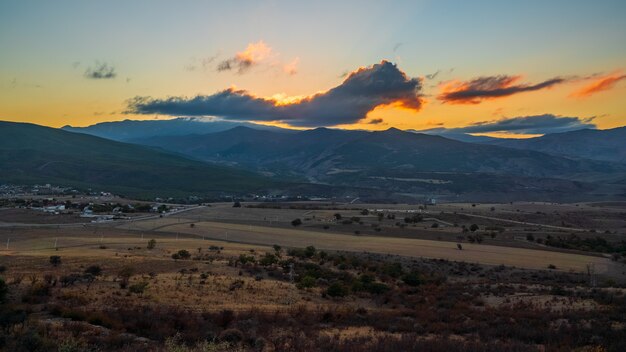 Pôr do sol colorido sobre as montanhas. Panorama amplo com vista para a vila e campos agrícolas