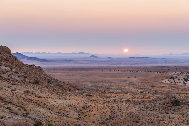 Por do sol colorido sobre o deserto de Namib, Aus, Namíbia, África. Céu claro violeta vermelho alaranjado no horizonte, rochas brilhantes e canyon em primeiro plano.