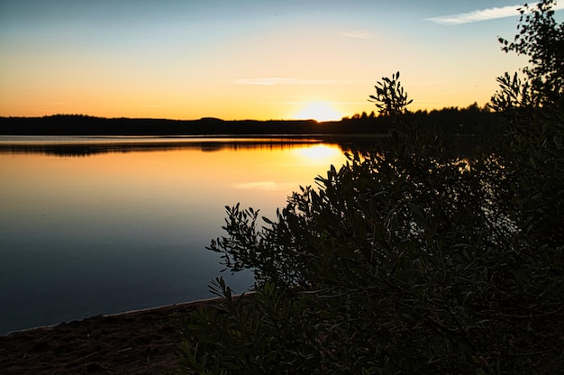 Pôr do sol com reflexo em um lago sueco em Smalland com arbustos em primeiro plano