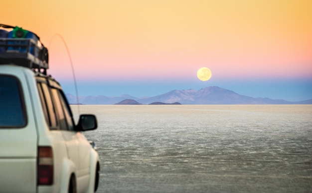 Pôr do sol da lua cheia com veículo de jipe fora de estrada em Salar De Uyuni World famoso lugar maravilhoso na Bolívia