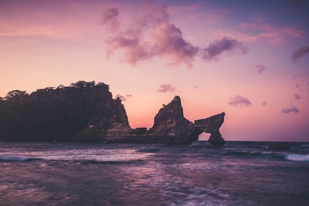 Pôr do sol do litoral da ilha de Nusa Penida da praia de Atuh. Floresta tropical na montanha e à beira-mar. Foto panorâmica na rocha e ondas do mar. Paisagem costeira em dias de bom tempo e céu nublado