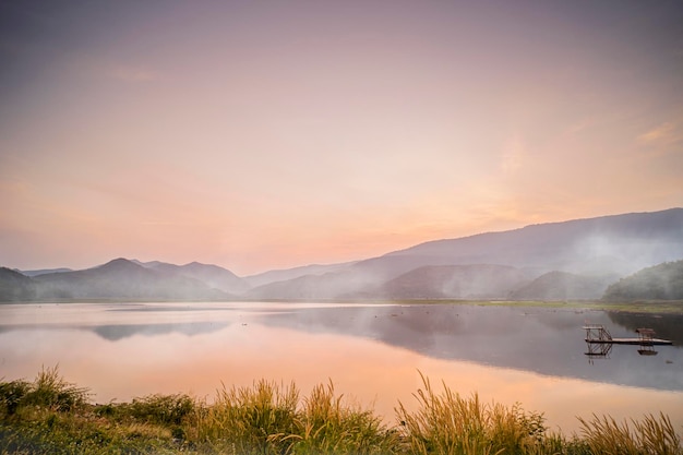 Por do sol dramático idílico com a cena de neblina sobre as montanhas do lago no fundo a