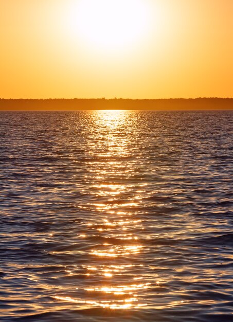 Pôr do sol e a trilha do sol na superfície do lago de verão.