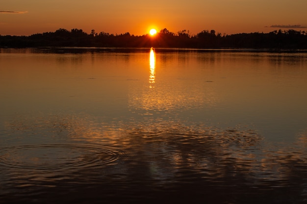 Pôr do sol ensolarado colorido em um lago calmo. o sol é refletido na superfície da água.